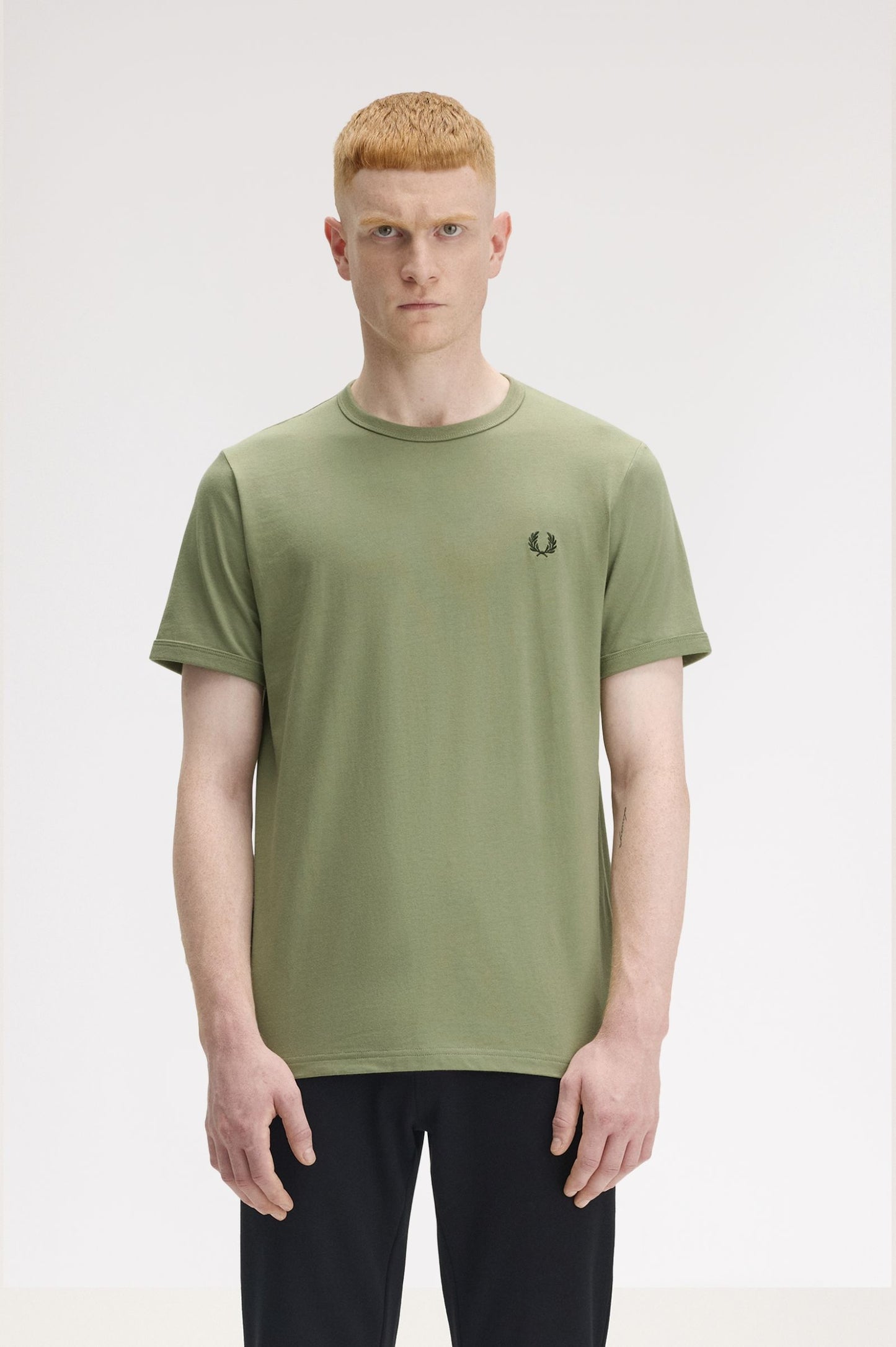 A person wearing a green Fred Perry ringer t-shirt with a logo on the chest.