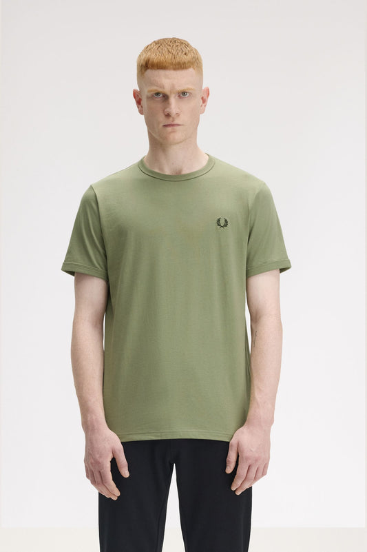 A person wearing a green Fred Perry ringer t-shirt with a logo on the chest.