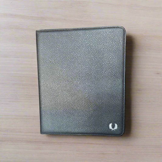 A brown scotch grain leather tablet case by Fred Perry, closed and placed on a wooden surface.
