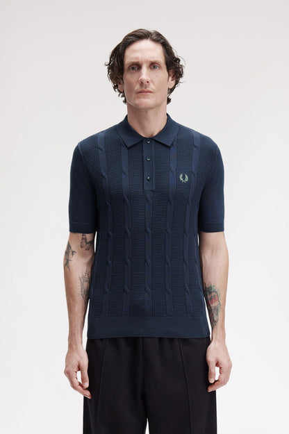 Man wearing a navy patterned polo shirt with a visible brand logo on a light background