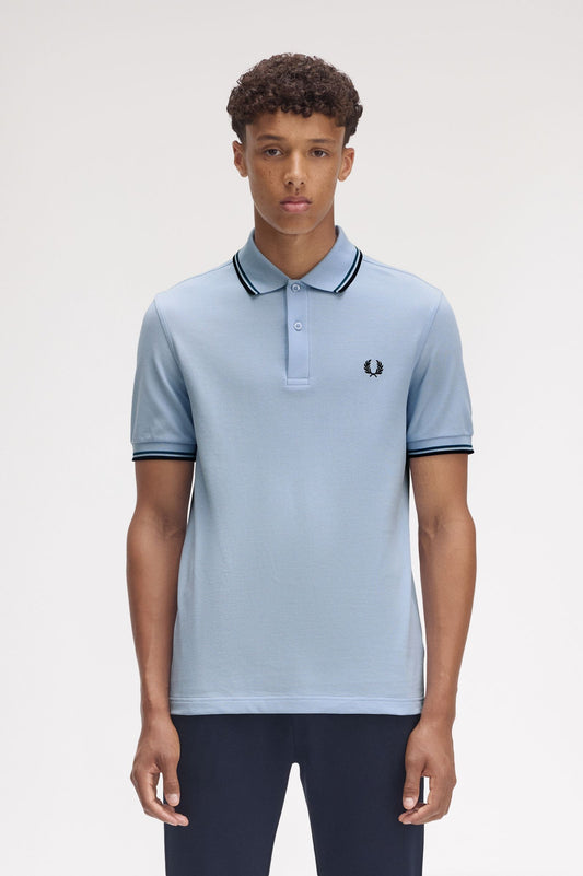 Person wearing a light blue polo shirt with dark trim on a plain background