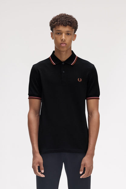 A man wearing a brown Fred Perry twin tipped polo shirt with white trim on the collar and sleeves, paired with white pants.