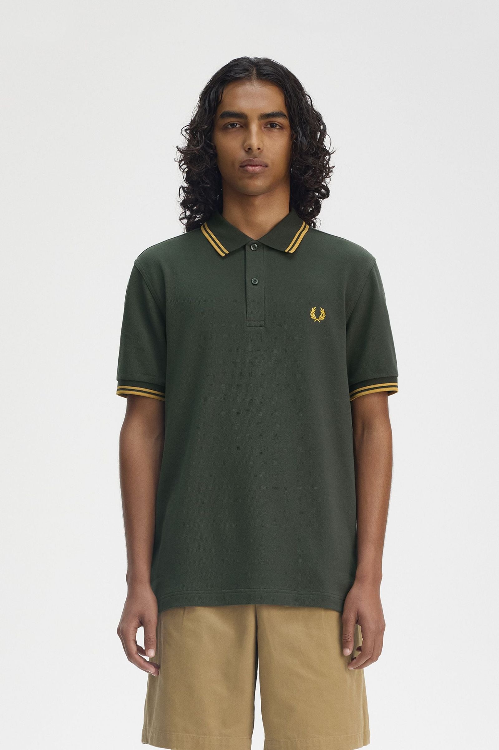 A male model wearing a green Fred Perry twin tipped shirt with collar and sleeve details.