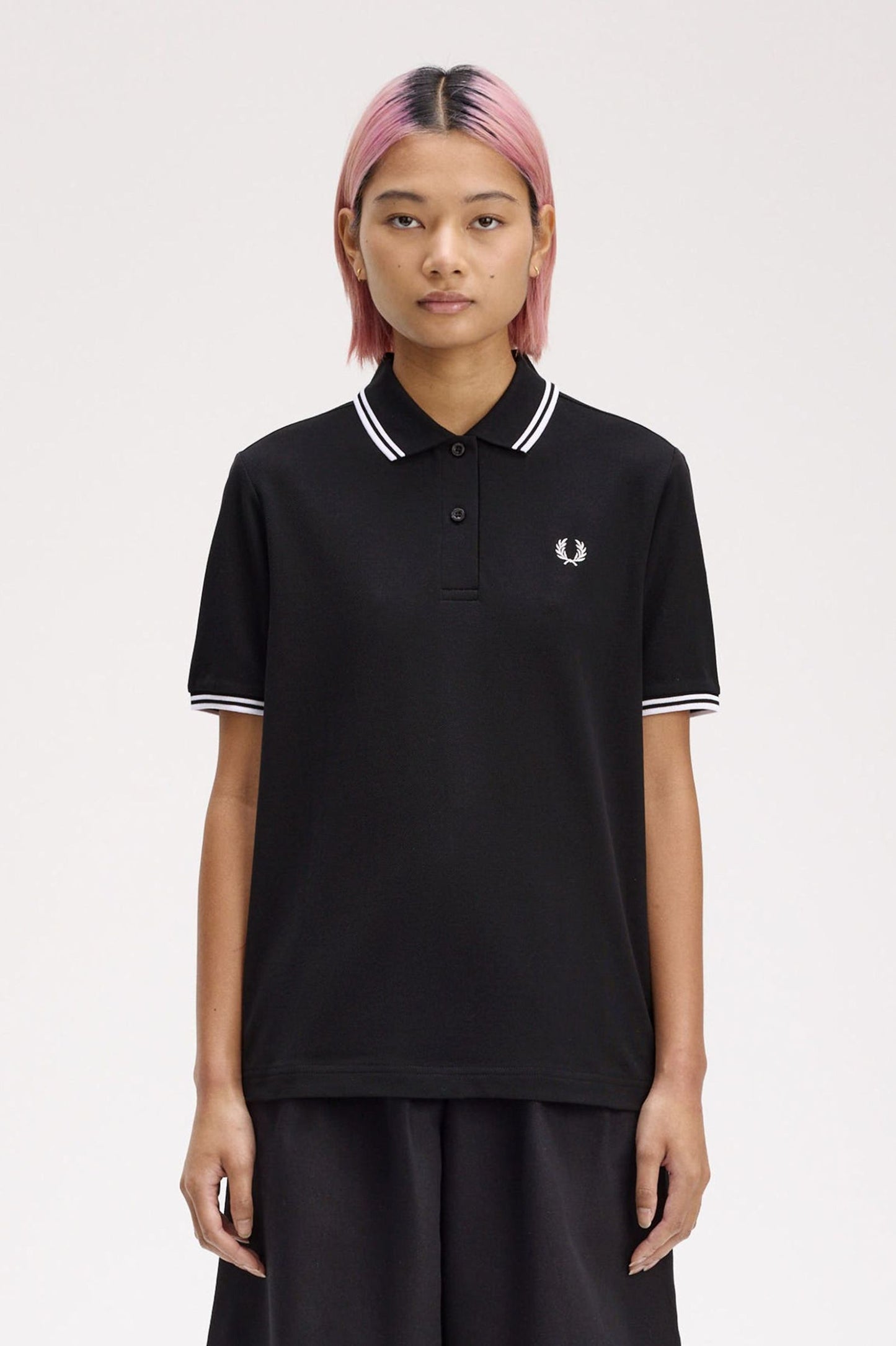 A person wearing a black Fred Perry twin tipped shirt with white collar and tipping, paired with dark pants.