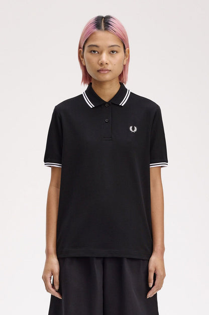 A person wearing a black Fred Perry twin tipped shirt with white collar and tipping, paired with dark pants.