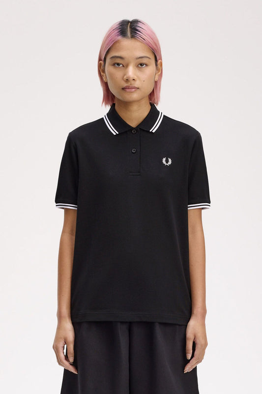 A person wearing a black Fred Perry twin tipped shirt with white collar and tipping, paired with dark pants.