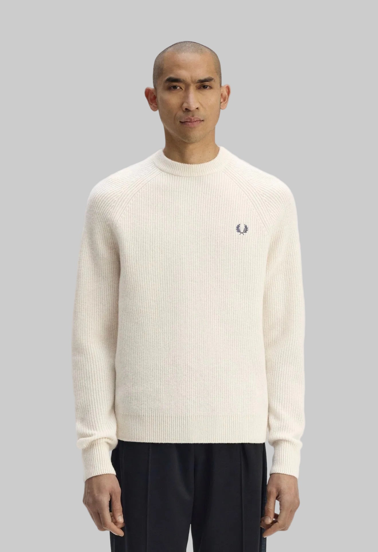 Man wearing a cream sweater with a brand logo on a white background