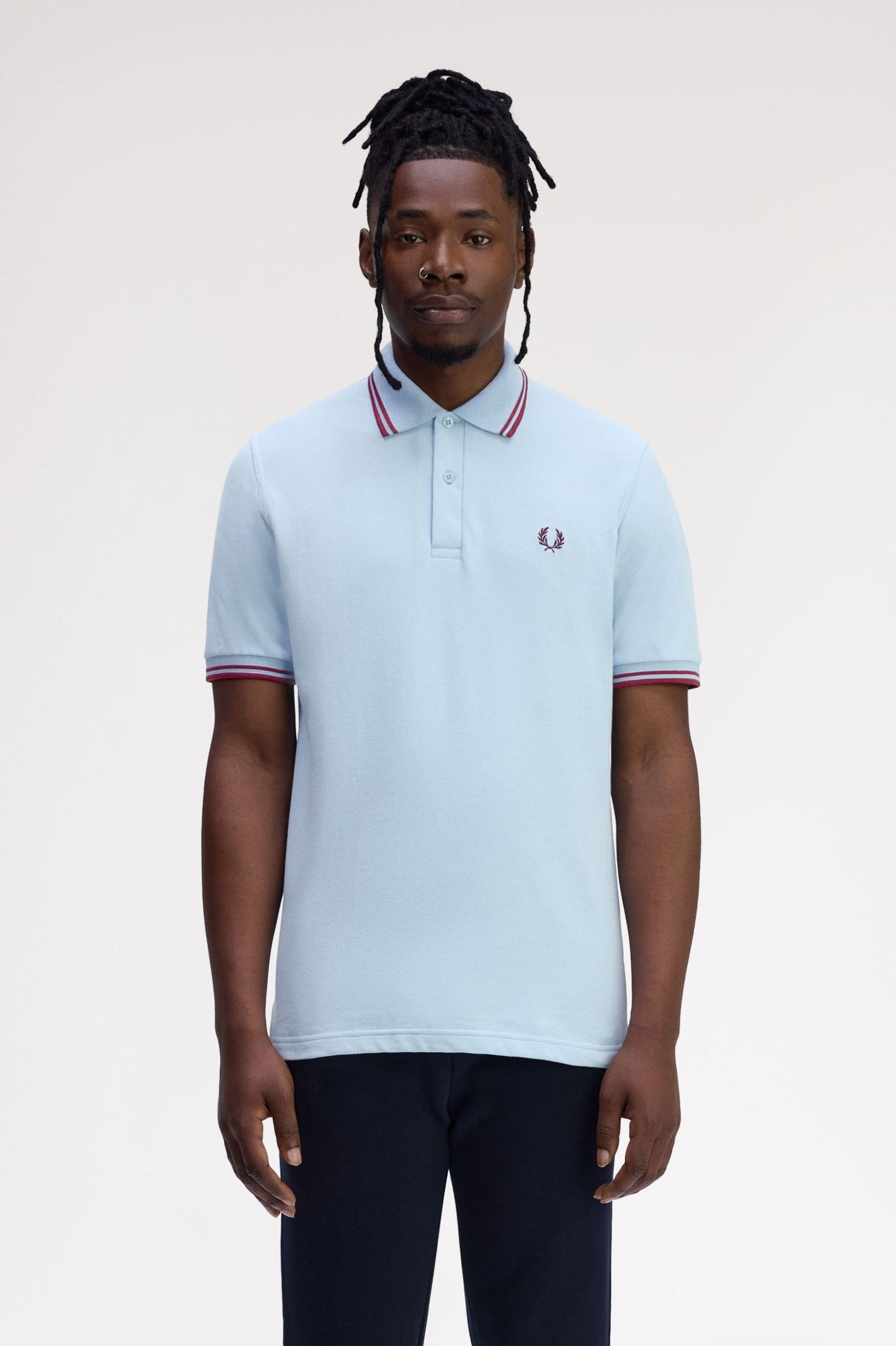 Man wearing a light blue polo shirt with red and white trim on a plain background