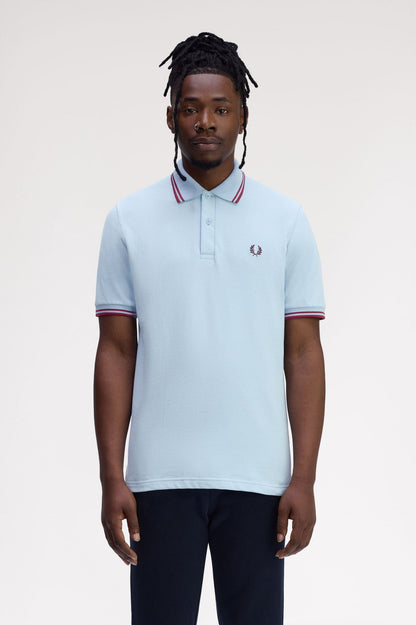 Man wearing a light blue polo shirt with red and white trim on a plain background