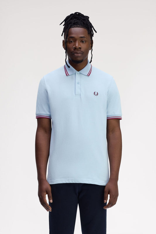 Man wearing a light blue polo shirt with red and white trim on a plain background