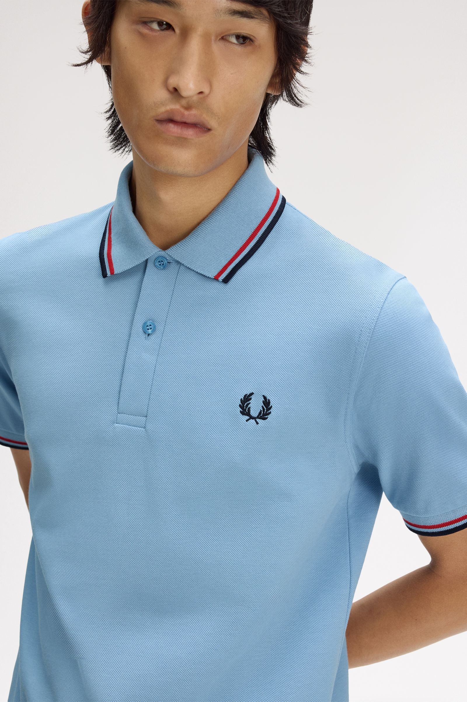 Man wearing a light blue polo shirt with a brand logo on a plain background