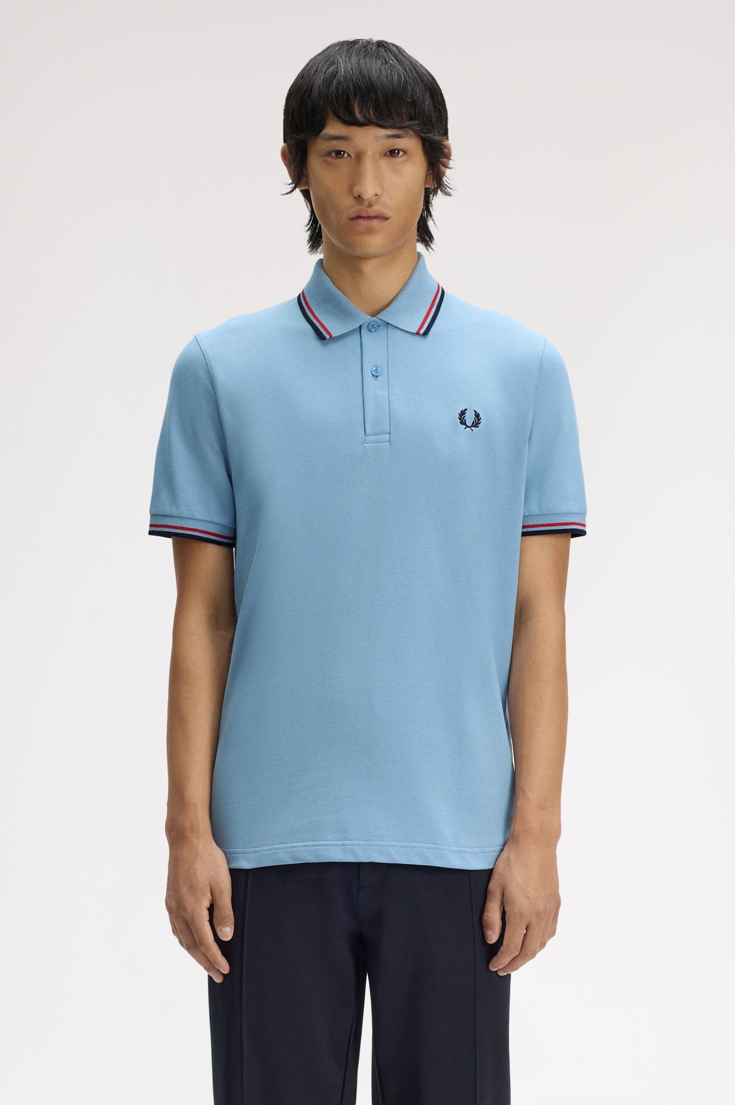 Person wearing a light blue polo shirt with a brand logo on a white background