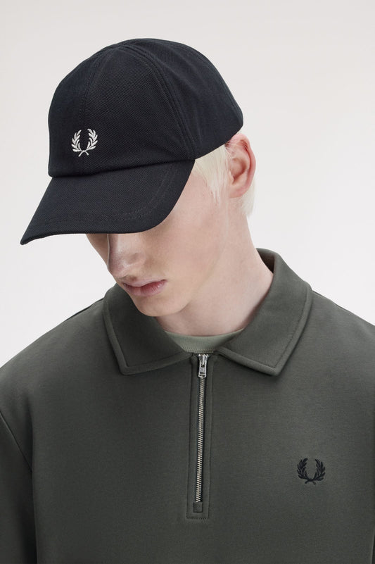 Person wearing a black Fred Perry cap and dark gray sweater with brand logo on a light gray background