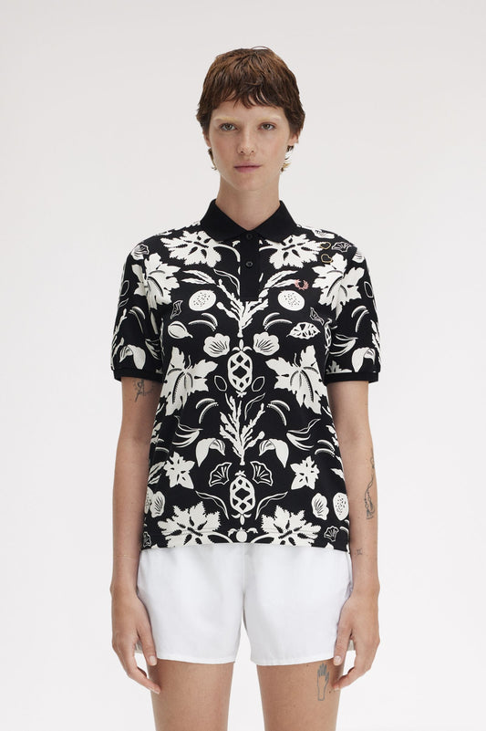 A person wearing a black and white floral printed Fred Perry shirt with short sleeves, paired with white shorts.