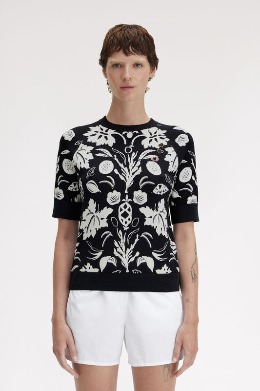 A woman wearing a black and white floral printed knitted top with short sleeves, paired with white shorts.