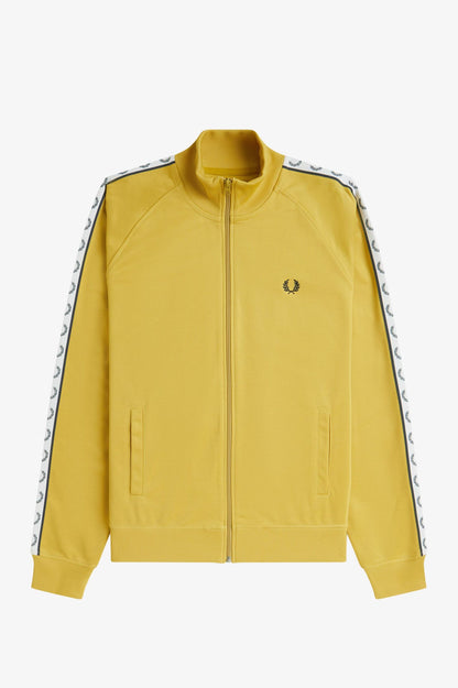 A person wearing a yellow Fred Perry track jacket with black tape on the arms and a hood, paired with dark shorts.