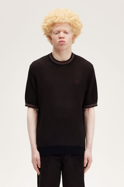 A male model wearing a black textured knitted t-shirt with a crew neck and two-tone construction. The shirt is displayed on a white background.