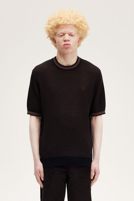 A male model wearing a black textured knitted t-shirt with a crew neck and two-tone construction. The shirt is displayed on a white background.