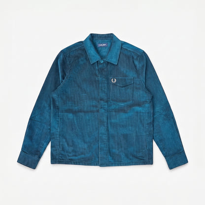 A blue corduroy button-up shirt jacket by Fred Perry, featuring a chest pocket with the signature laurel wreath logo, laid flat against a white background.