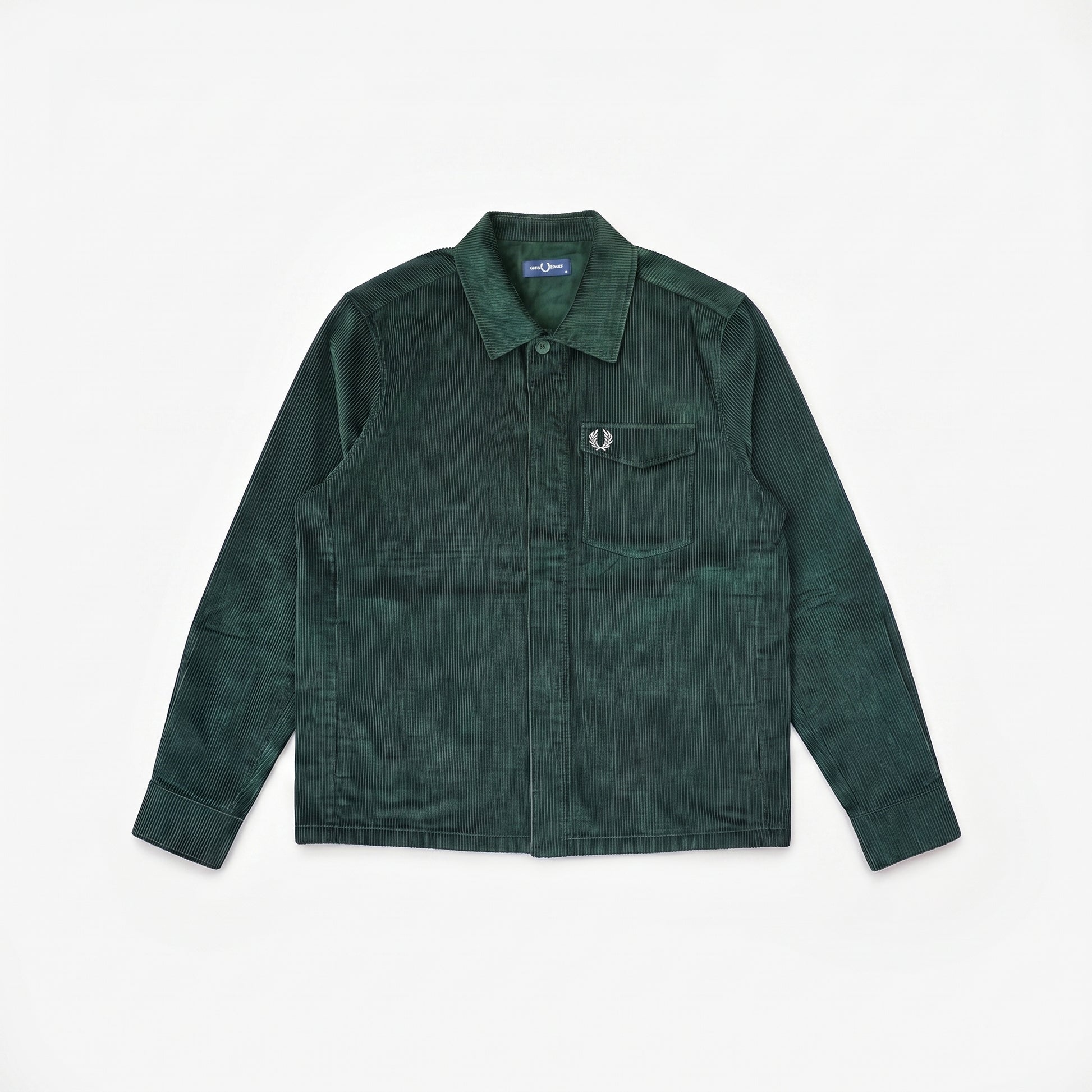 A dark green corduroy utility shirt jacket with a pointed collar, button-up front, and a chest pocket featuring a signature Fred Perry laurel wreath emblem, laid flat on a white background.