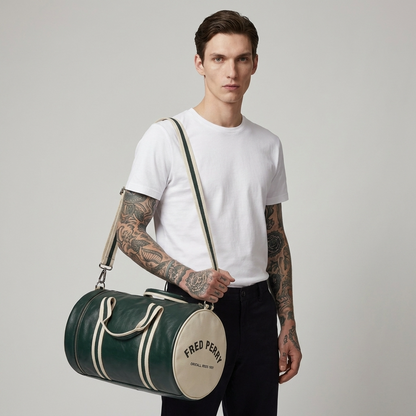 A man wearing a white t-shirt and black pants carries a green and cream duffel bag with 'FRED PERRY' printed on the front, set against a plain light gray background.