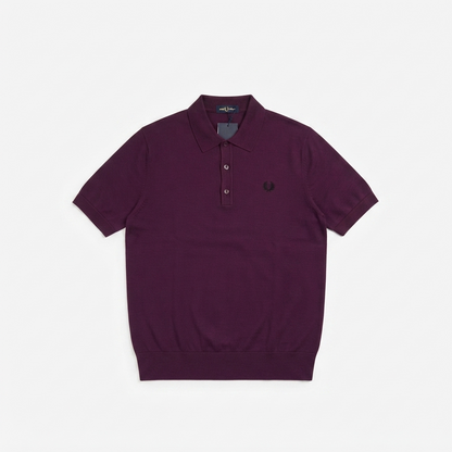A short-sleeve polo shirt in deep plum purple, featuring a three-button placket and the signature embroidered laurel leaf logo on the left chest, displayed flat against a light gray background.