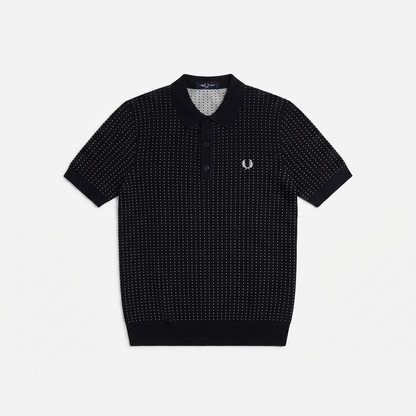 A short-sleeve polo shirt by Fred Perry featuring a black and white micro-dot pattern, a classic collar, and the signature embroidered laurel wreath logo on the left chest, displayed flat against a light gray background.
