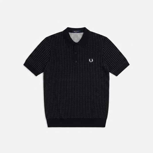 A short-sleeve polo shirt by Fred Perry featuring a black and white micro-dot pattern, a classic collar, and the signature embroidered laurel wreath logo on the left chest, displayed flat against a light gray background.