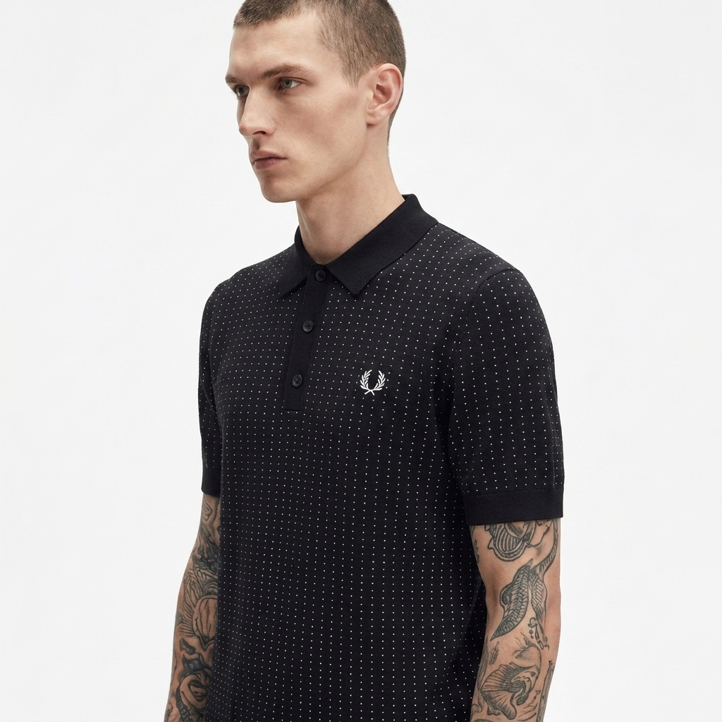 A man wearing a black short-sleeve polo shirt with a fine white micro-dot pattern and the iconic silver embroidered laurel wreath logo on the chest, set against a plain light gray background.