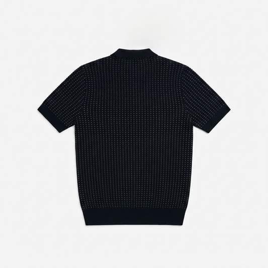 A short-sleeve knit polo shirt shown from the back, featuring a dark navy base with a dense pattern of tiny white dots, photographed flat against a light gray background.