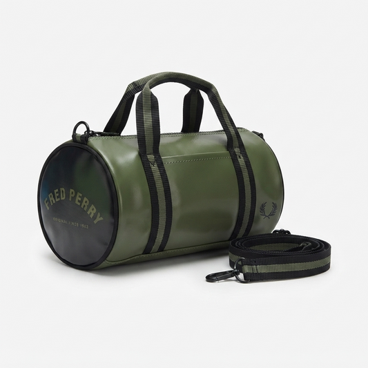 An olive green cylindrical duffel bag with black handles and side stripes, featuring a black circular end cap with gold 'FRED PERRY' branding and a matching black-and-green shoulder strap on a light gray background.