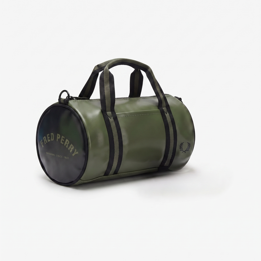 An olive green cylindrical duffel bag by Fred Perry, featuring black webbing handles, black side stripes, and a black circular end cap with gold lettering, set against a plain white background.