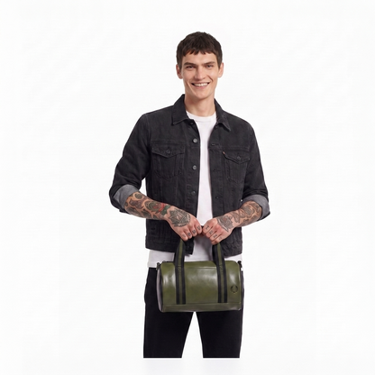 A model wearing a black denim jacket and white t-shirt holds an olive green cylindrical duffel bag with black handles against a plain white background.