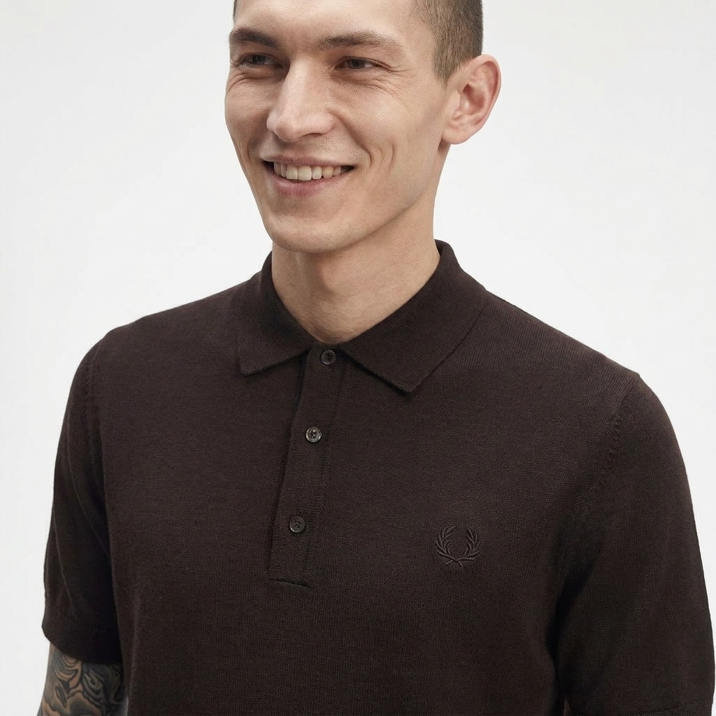 A man wearing a dark brown short-sleeve polo shirt with a three-button placket and a small embroidered logo on the left chest, photographed against a plain light background.