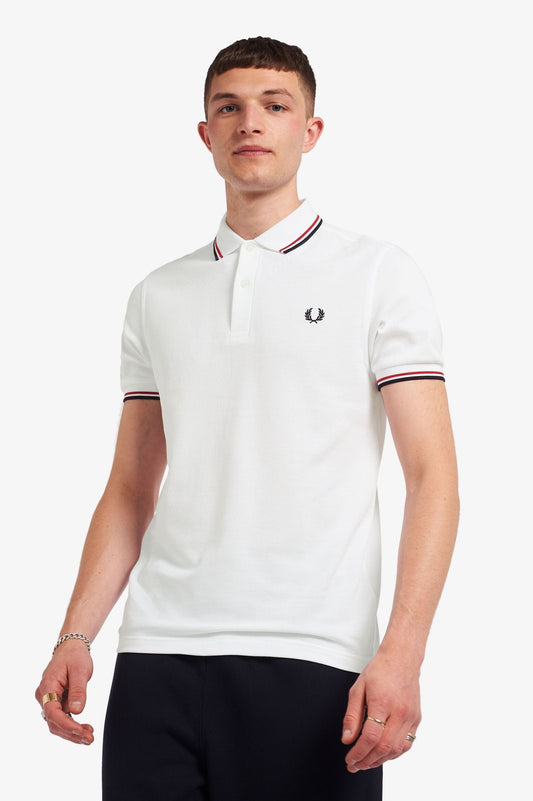 A man wearing a white Fred Perry Twin Tipped polo shirt with red and blue tipping on the collar and cuffs.