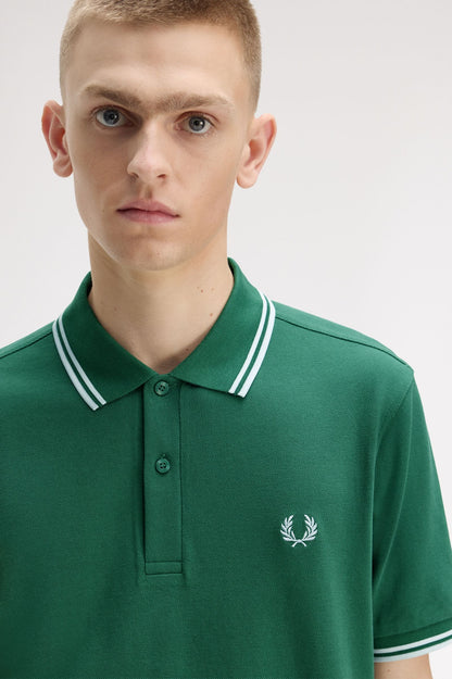 Man wearing a green polo shirt with a brand logo on a white background