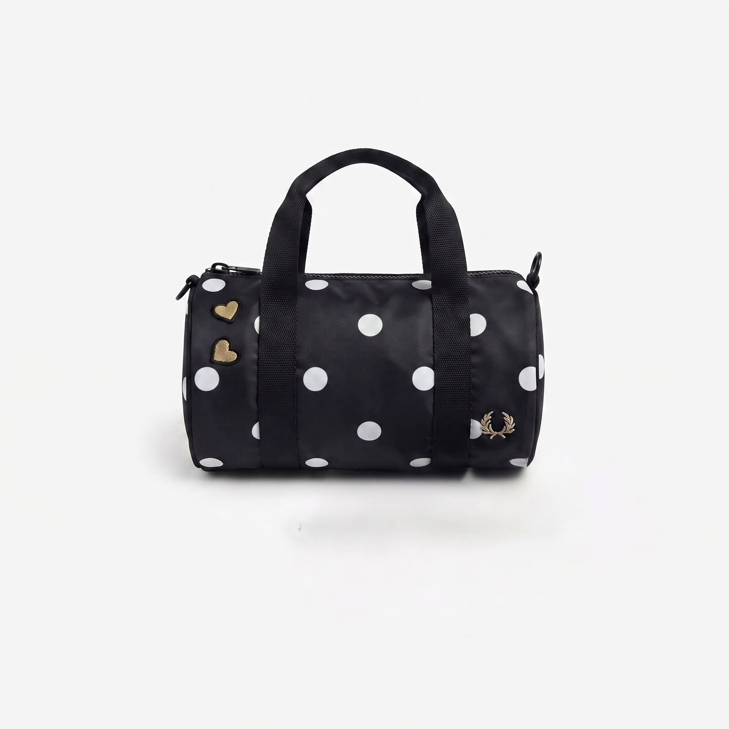 A black nylon duffel bag with white polka dots, featuring a top handle, gold heart charms on the zipper, and a small gold embroidered logo on the front.