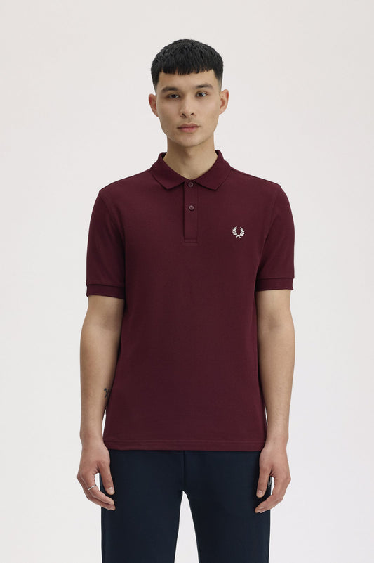 Person wearing a maroon polo shirt with a brand logo on a white background