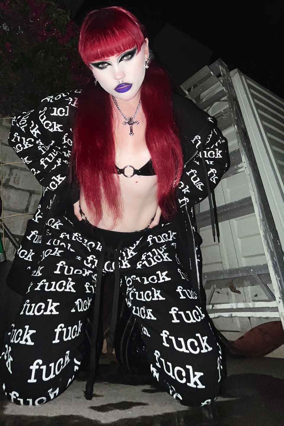 Person wearing a lip service black outfit with 'fuck' text, standing in an indoor setting.