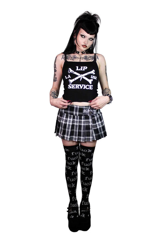 Person wearing a lip service black tank top with text, plaid skirt, and black stockings with text on a white background