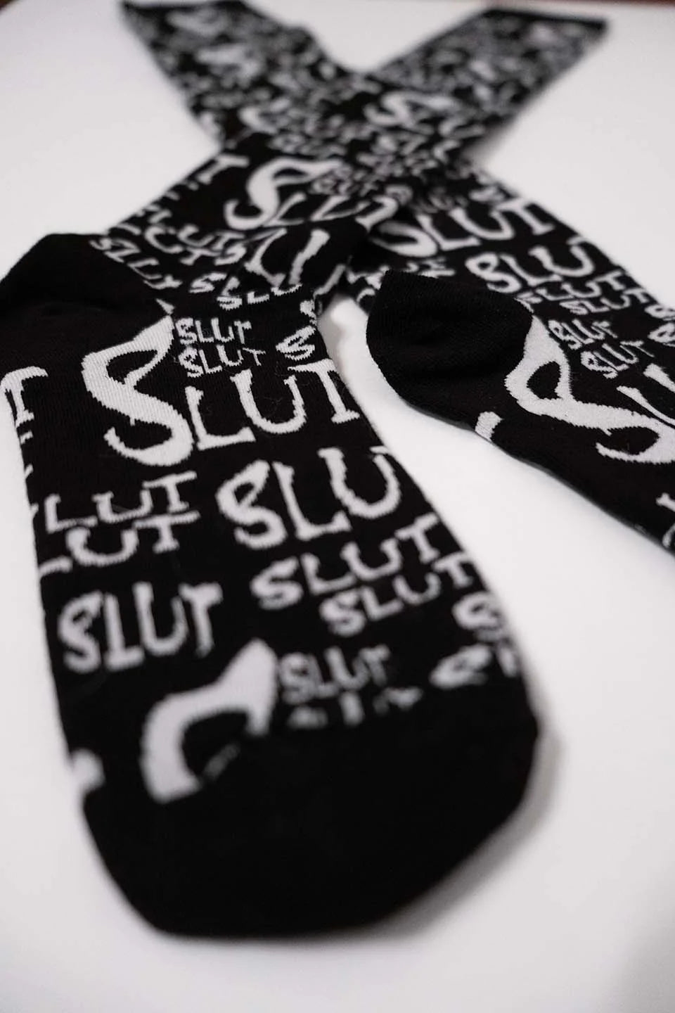 Black lip service socks with 'SLUT' printed in white on a white background
