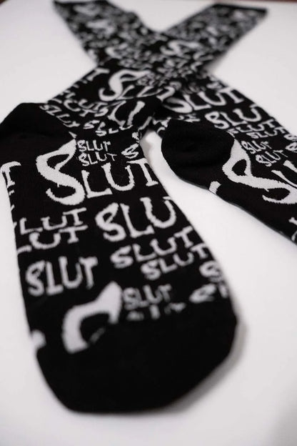 Black lip service socks with 'SLUT' printed in white on a white background