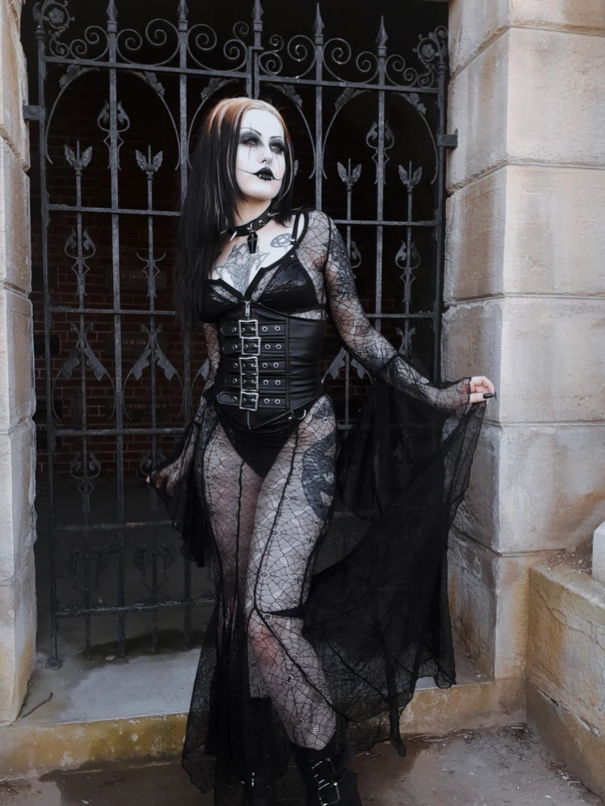 Person in a lip service  gothic costume standing in front of an ornate metal gate.